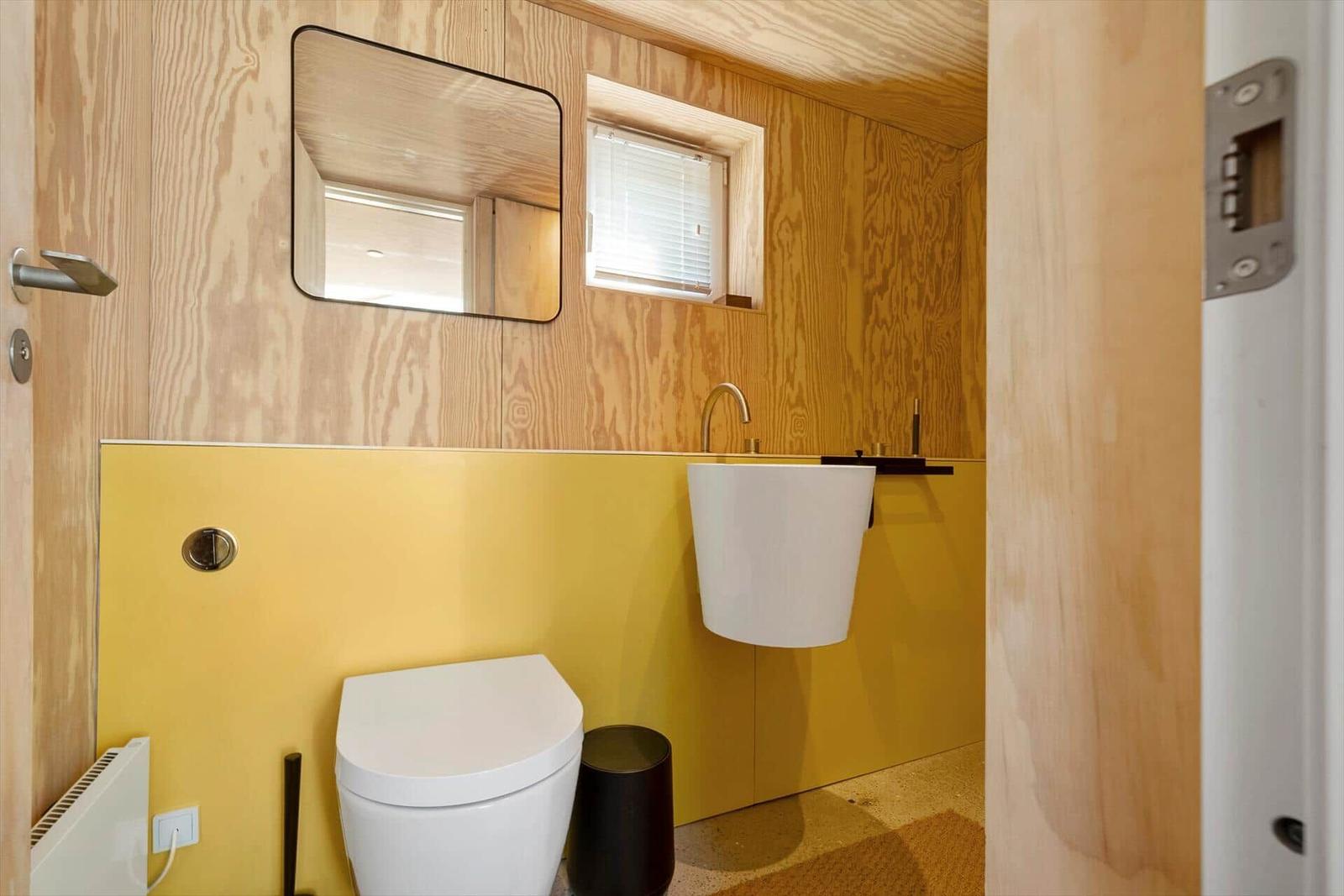 Badezimmer mit Toilette, Waschbecken und Spiegel an Holzwand.
