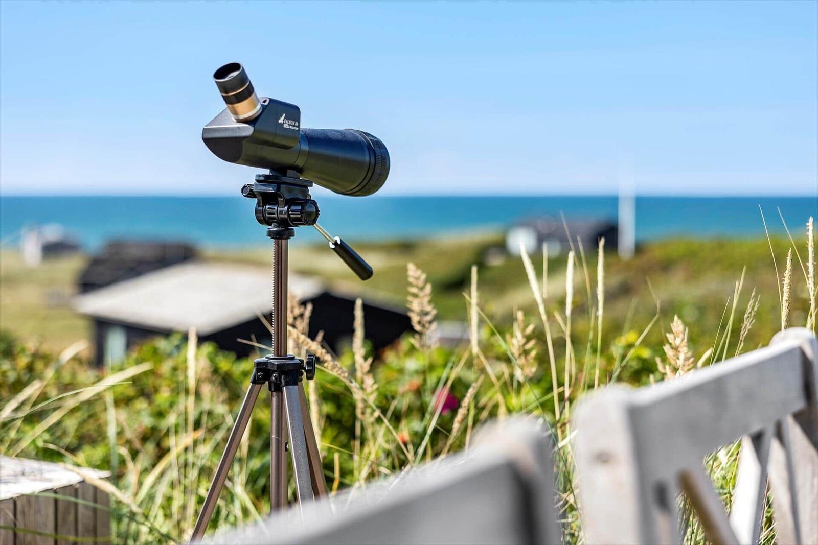 Ein Fernglas auf einem Stativ im Freien mit Blick auf das Meer und Gras.