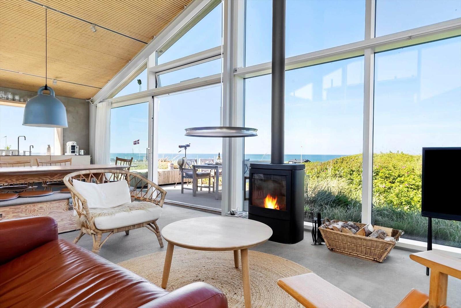 Wohnraum mit Kamin, großem Fenster und Meerblick. Möbel und Einrichtung sind sichtbar.