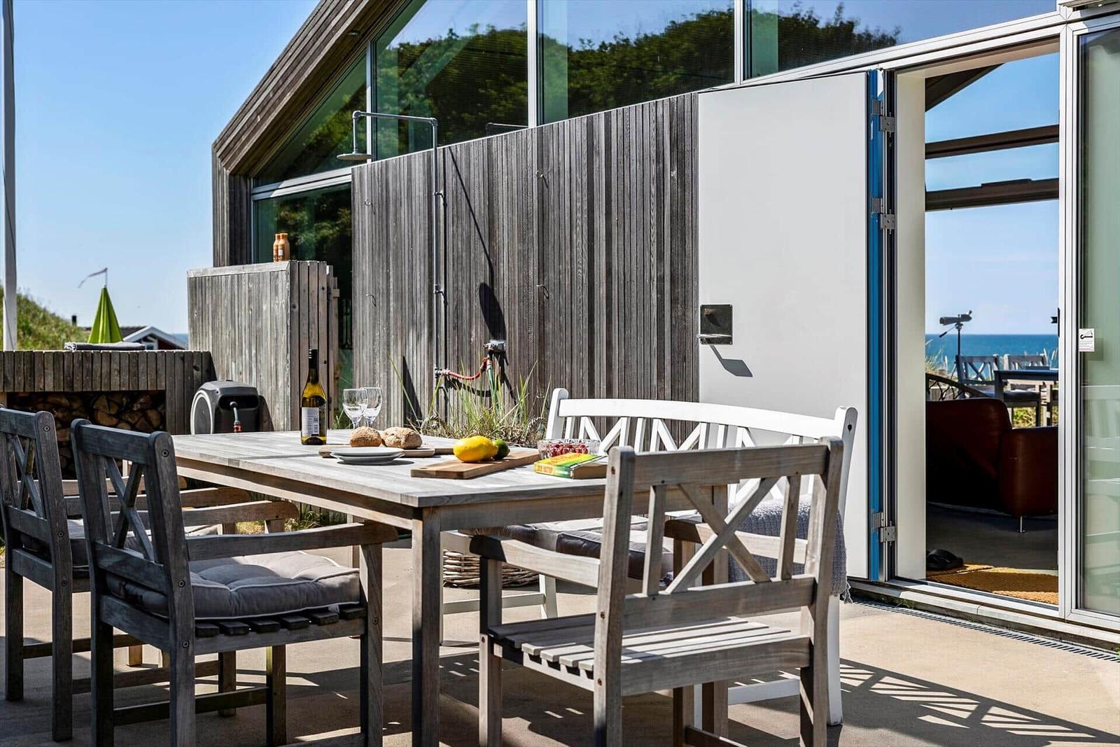 Terrasse mit Tisch, Stühlen und Grill. Durchgehendes Glasfenster zum Innenraum.