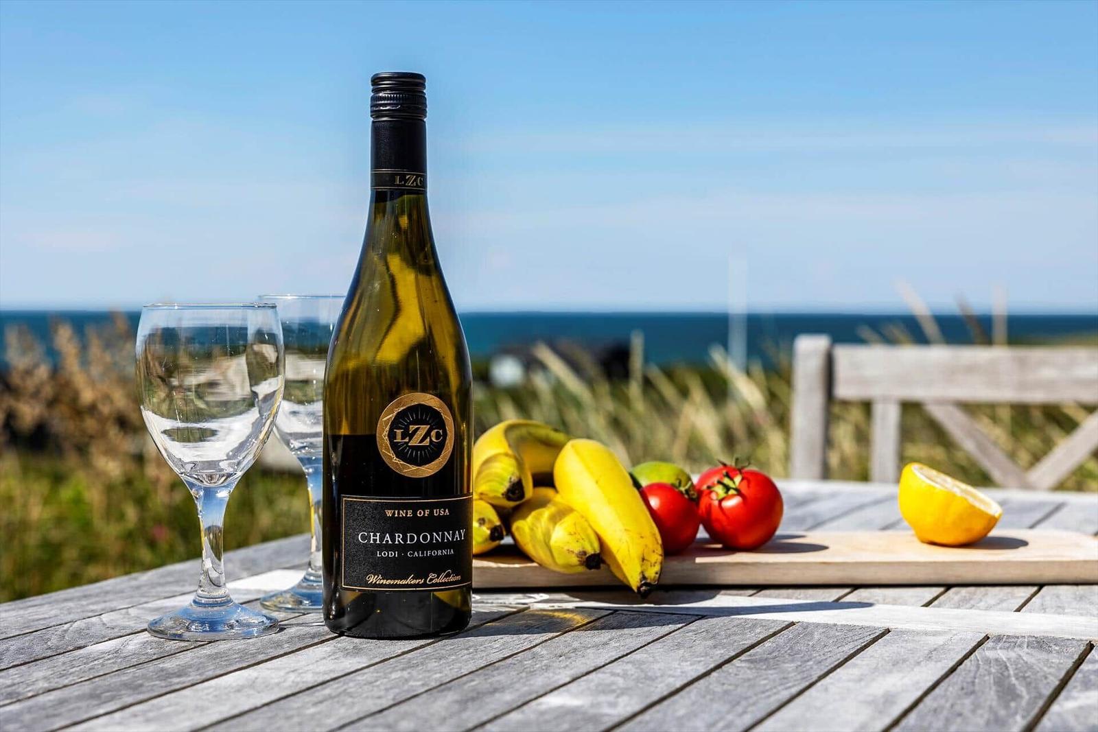 Weinflasche, Gläser und Obst auf Tisch mit Meerblick