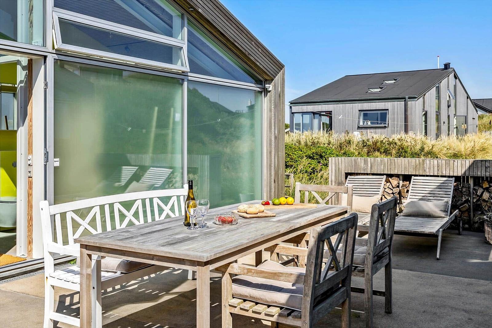 Terrasse mit Holztisch, Stühlen und Grillplatz. Im Hintergrund moderne Häuser.