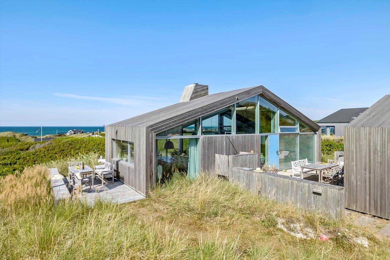 Moderne Strandhaus mit großem Glasbereich und Terrasse. Blick auf das Meer und Dünen.
