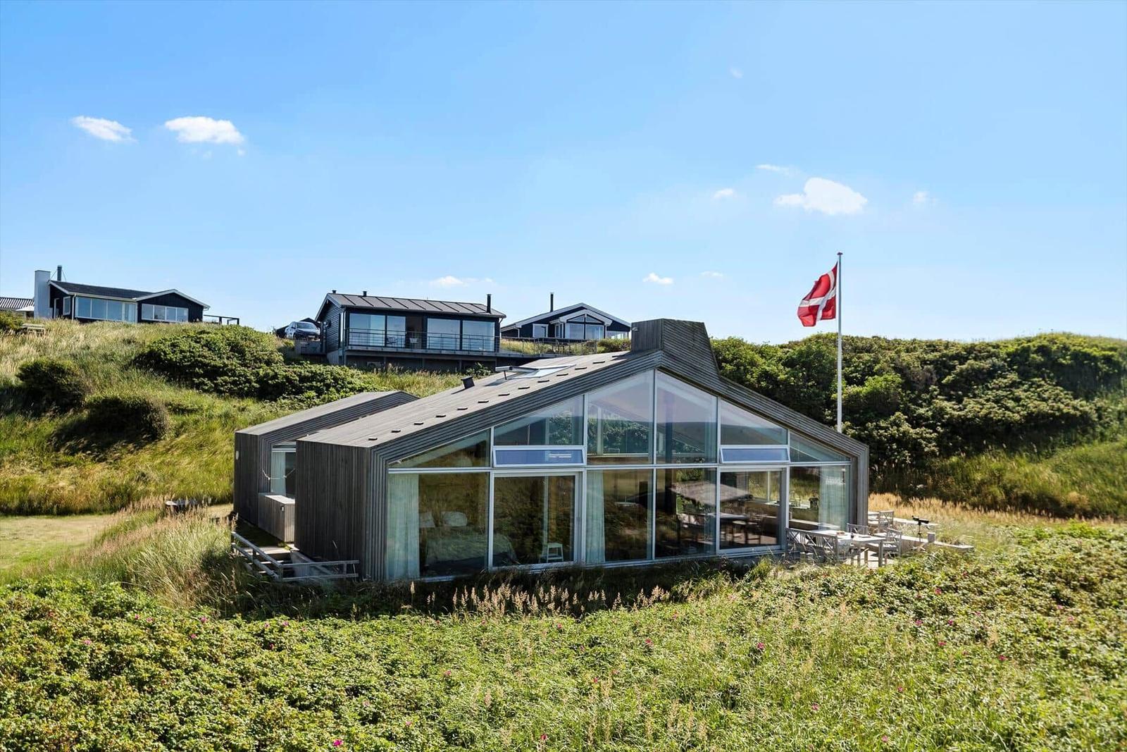 Moderne Villa mit großem Glasbereich, Flagge und Grünanlagen im Hintergrund.