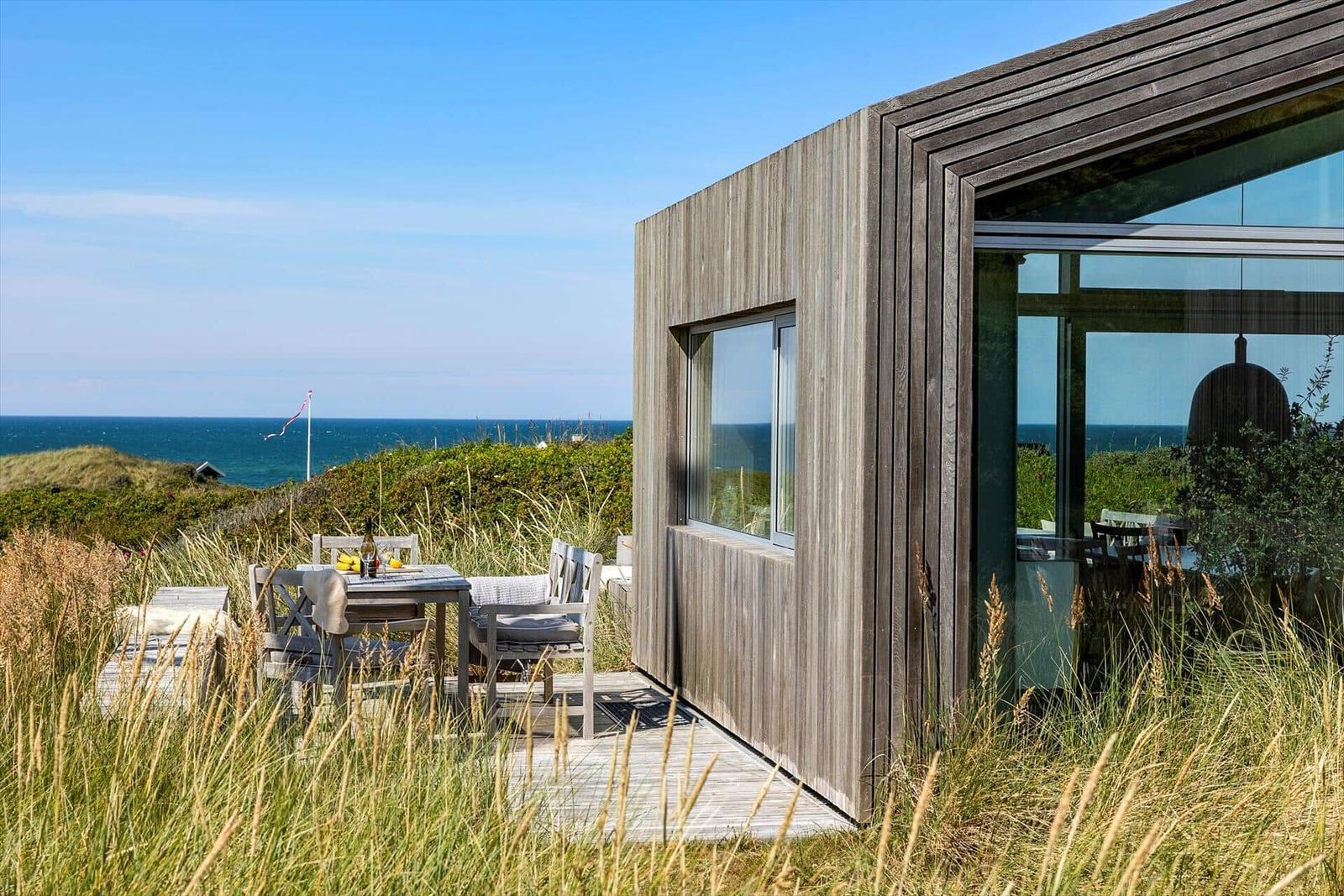 Moderne Strandhütte mit Terrasse und Meerblick. Holzwand und Glasfront.