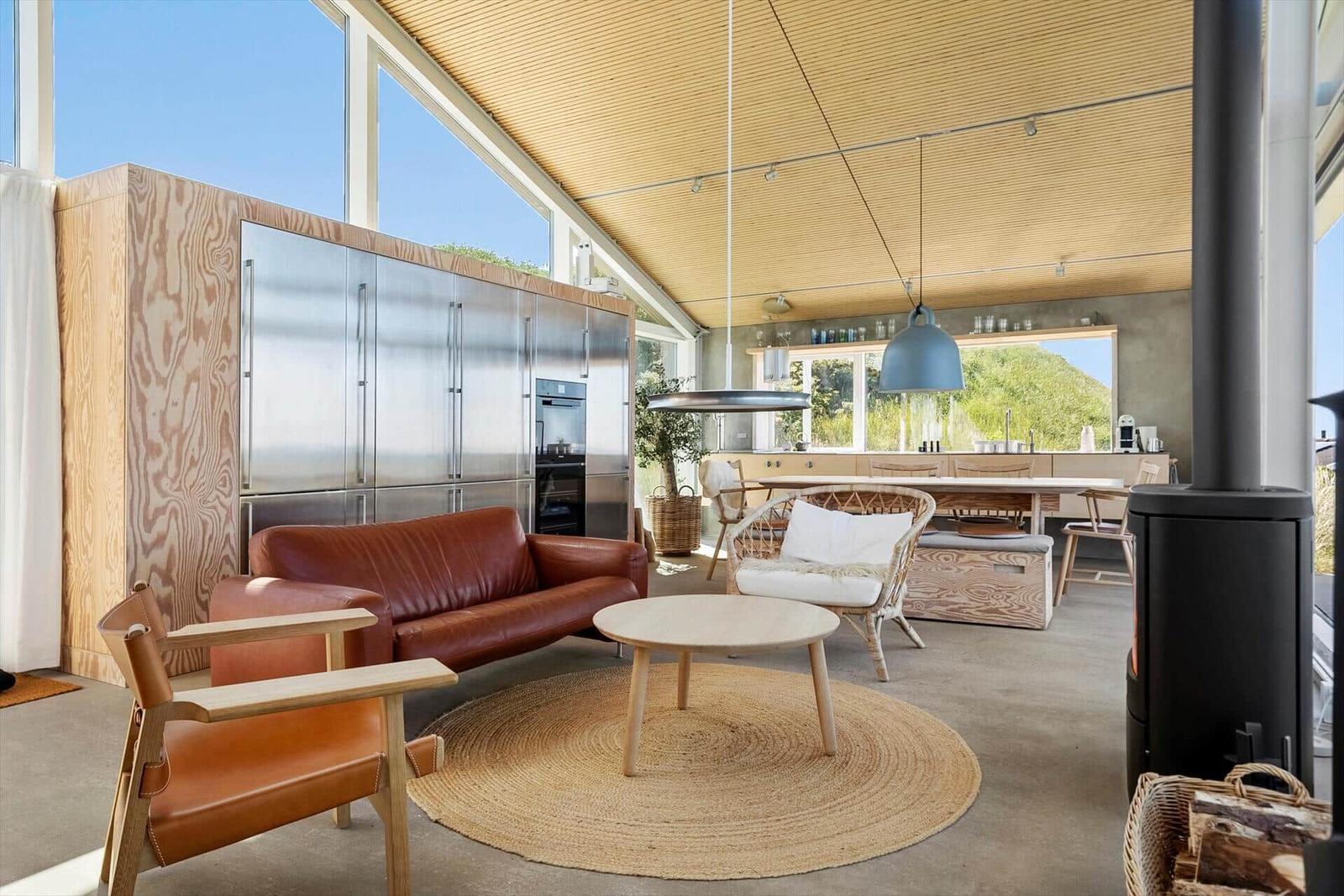 Wohnbereich mit Ledersofa, Esstisch und Küchenzeile. Holzdecke und große Fenster.