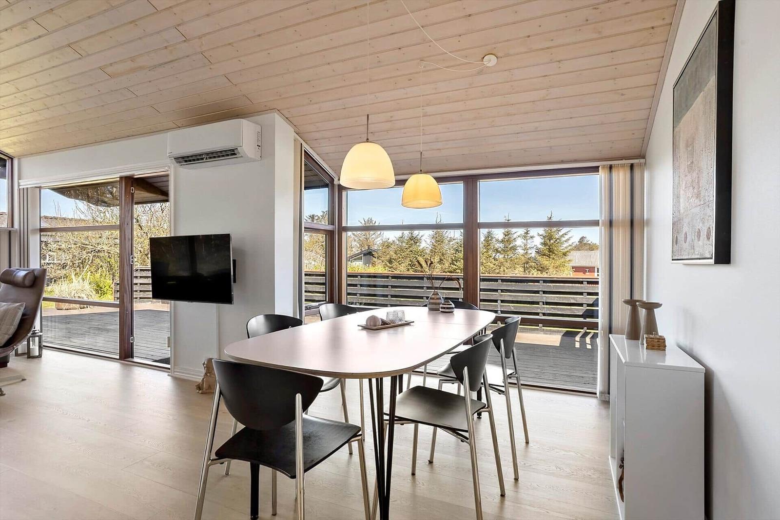 Essbereich mit Tisch und Stühlen, große Fenster und Holzdecke.