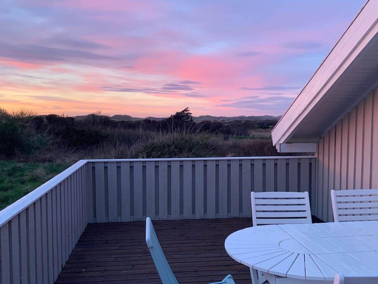 Terrasse mit Tisch und Stühlen bietet Blick auf Dünensandszene bei Sonnenuntergang.