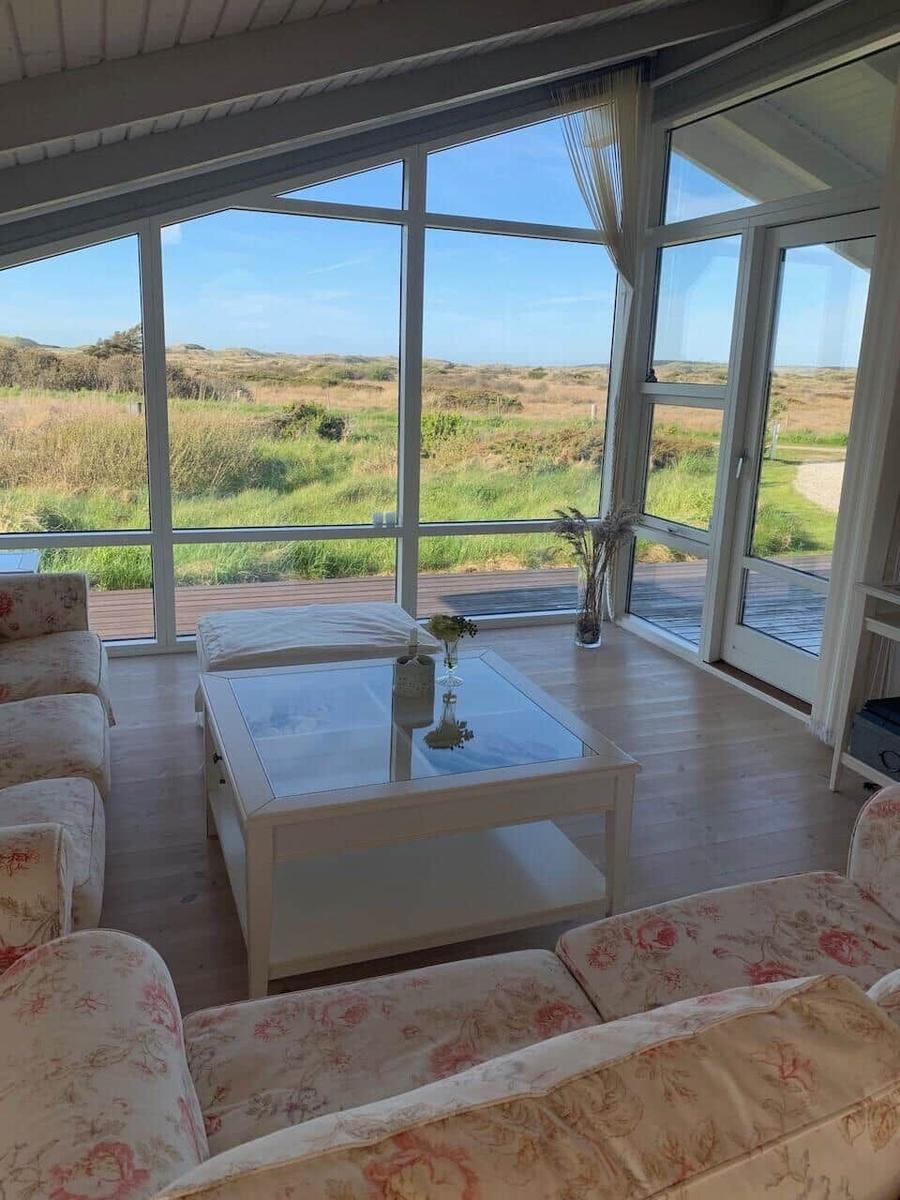 Wohnzimmer mit Blick auf Grasland durch große Fenster und Glas-Tisch.