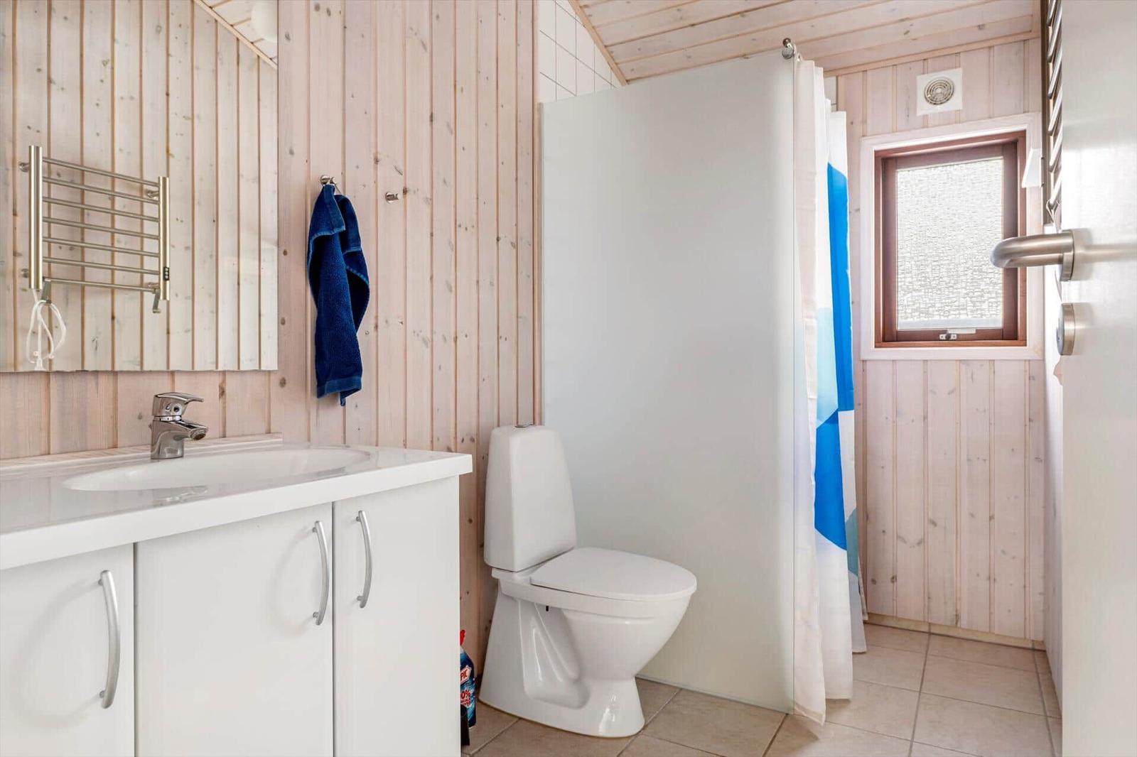 Badezimmer mit Waschbecken, Toilette und Dusche. Holzwände und Fenster mit Glasmosaik.