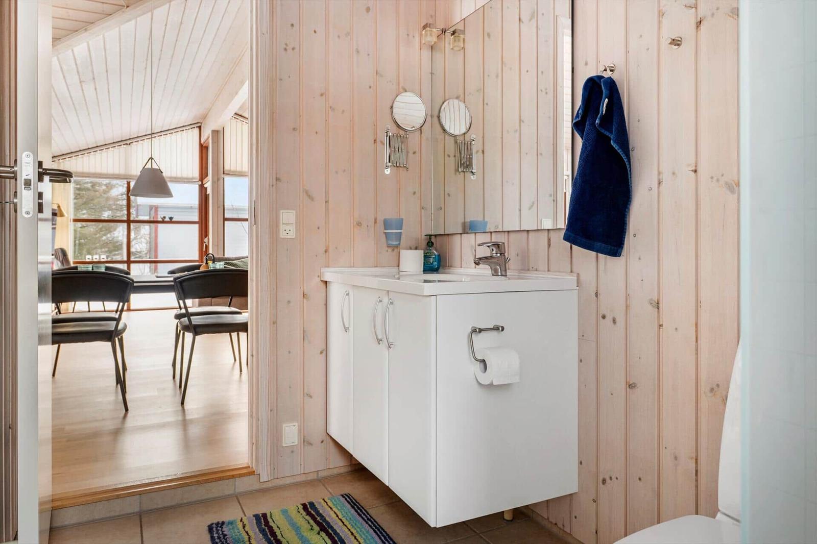 Badezimmer mit Waschbecken, Spiegel und blauem Handtuch an Holzwand