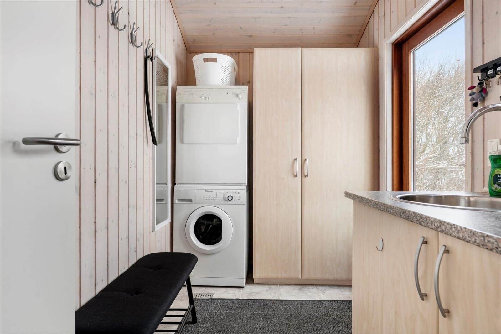 Waschraum mit Waschmaschine, Trockner und Schrank. Fenster mit Blick auf Bäume.