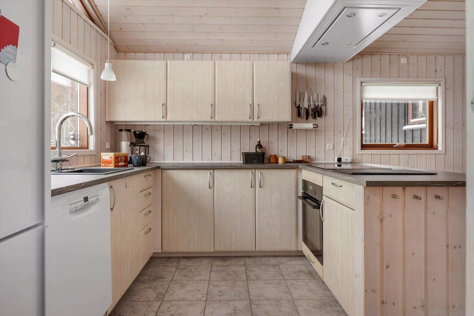 Küche mit Holzwand, hellen Schränken und Edelstahlspüle.