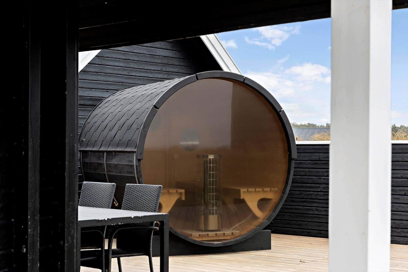 Außenliegende Sauna mit Sitzbänken und Tisch. Hintergrund: Holzwand und Himmel.