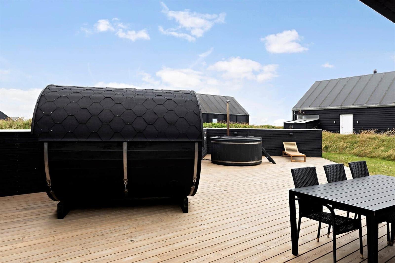Terrasse mit Sauna, Whirlpool und Esstisch. Hintergrund: moderne Gebäude und Grasfläche.