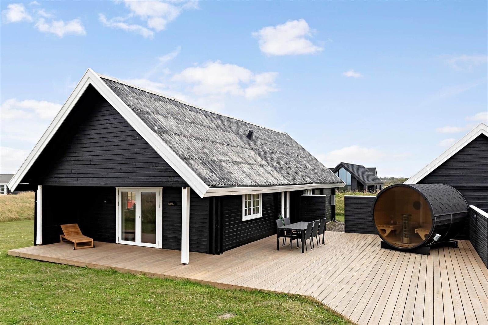 Schwarzes Holzhaus mit Terrasse, Liegestuhl und Sauna im Freien.