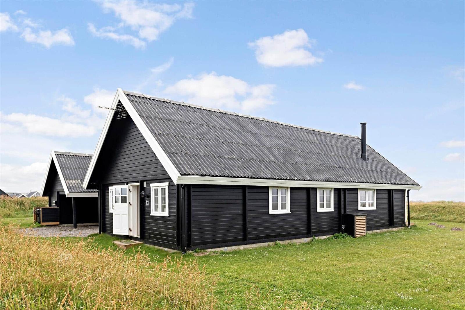 Schwarzes Holzhaus mit weißen Fenstern und Tür. Grasland im Hintergrund.