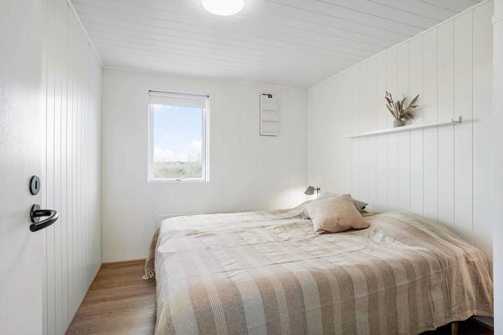 Schlafzimmer mit Bett, Fenster und weißen Wänden.