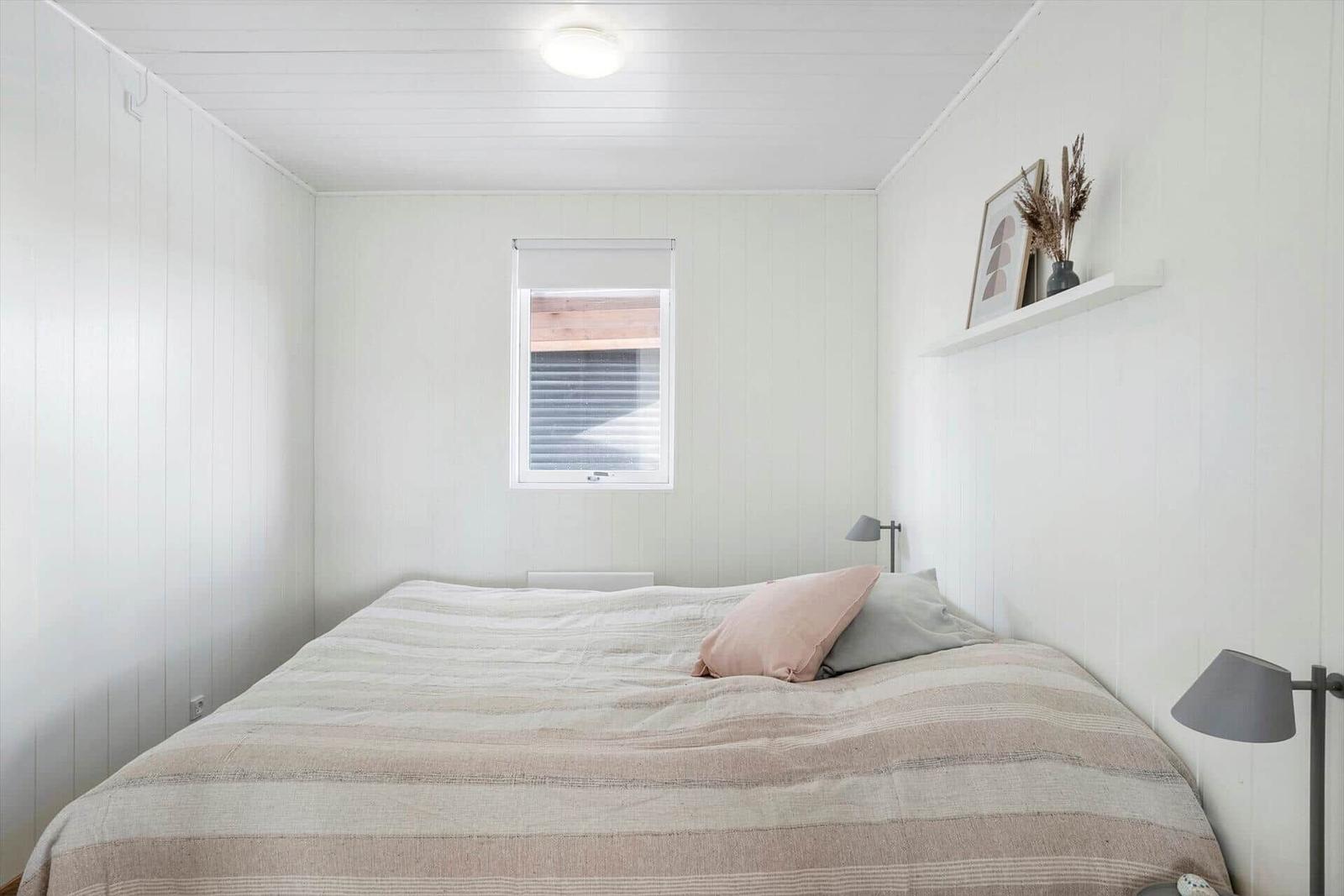 Schlafzimmer mit Bett, Fenster und Wandregal mit Dekoration.