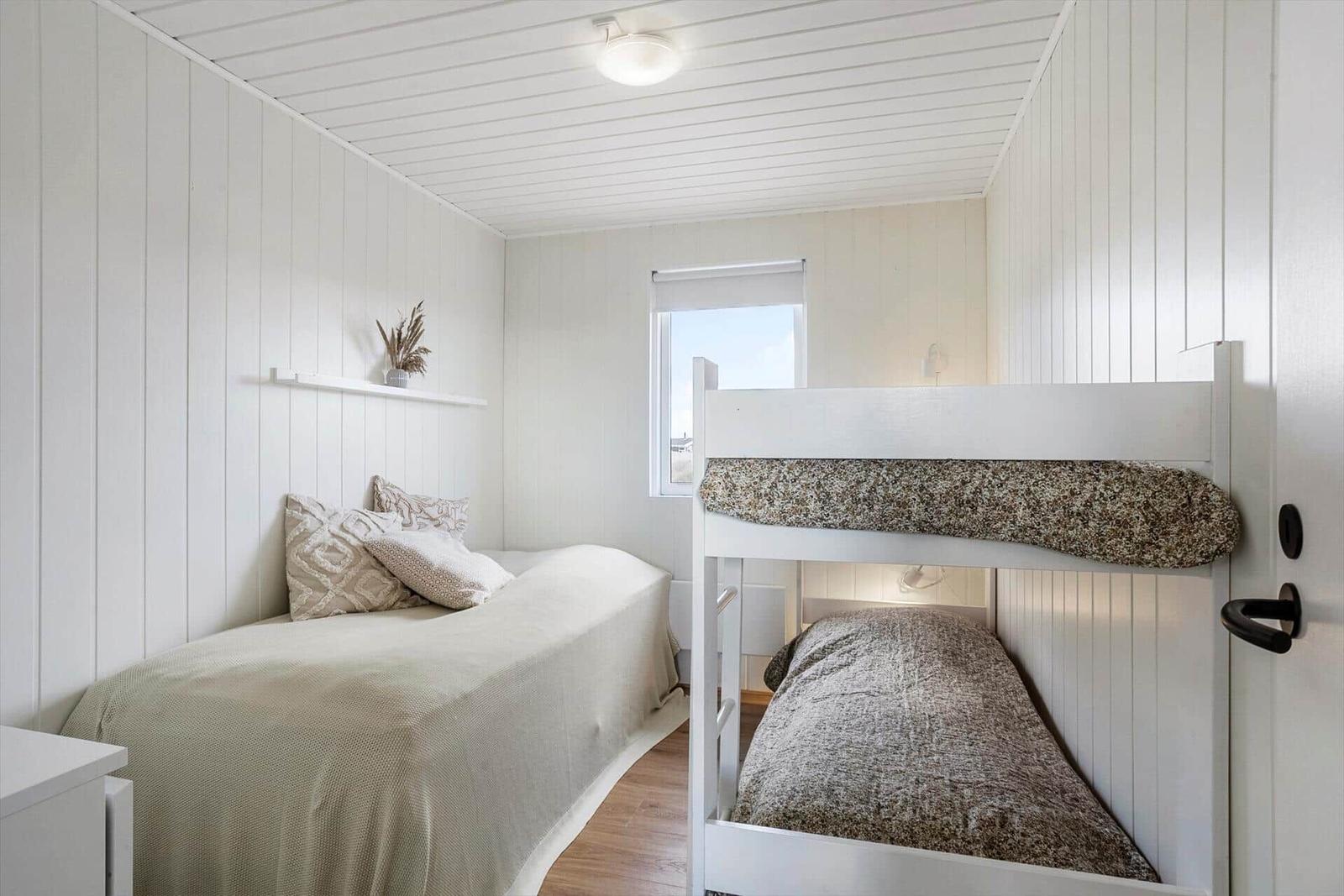 Schlafzimmer mit Einzelbett und Doppelstockbett. Weiße Wände und Holzboden.