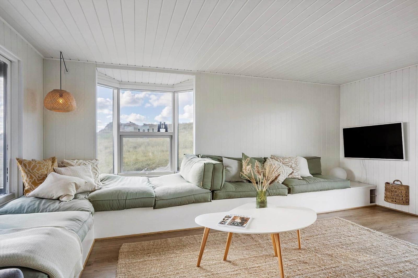 Wohnzimmer mit grünem Sofa, runden Tisch und Fernseher an der Wand.