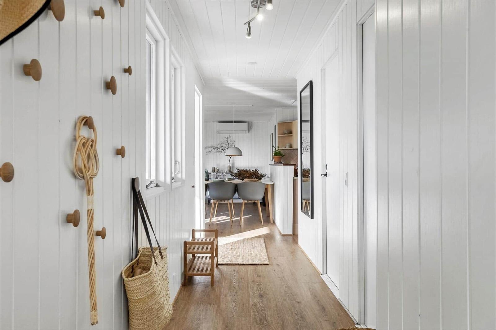 Flur mit Holzboden und weißen Wänden. An der Wand hängen Holzknöpfe und ein geflochtener Stab.