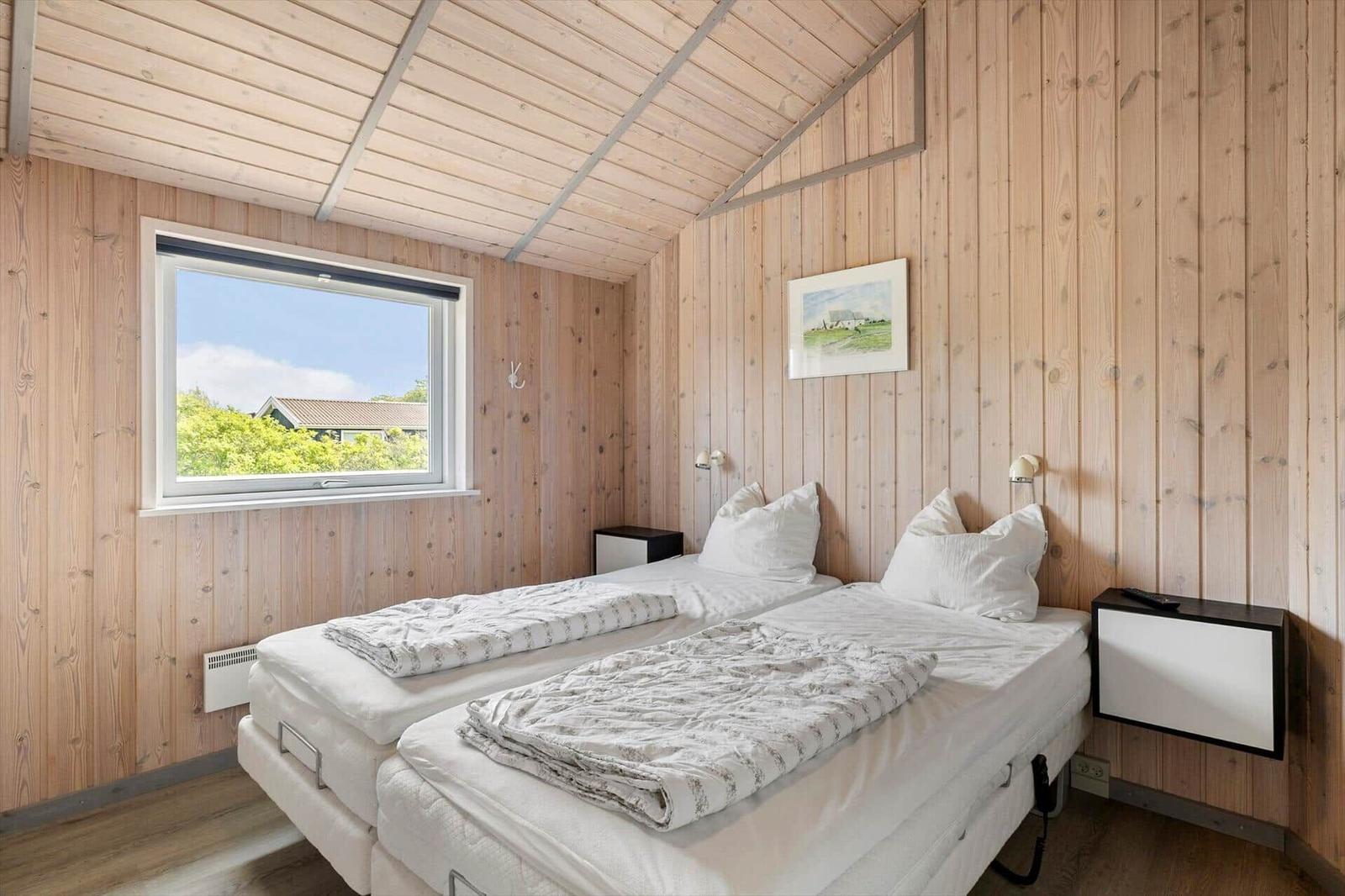 Zwei Einzelbetten in einem Holzhaus mit Fensterblick auf Grünflächen.