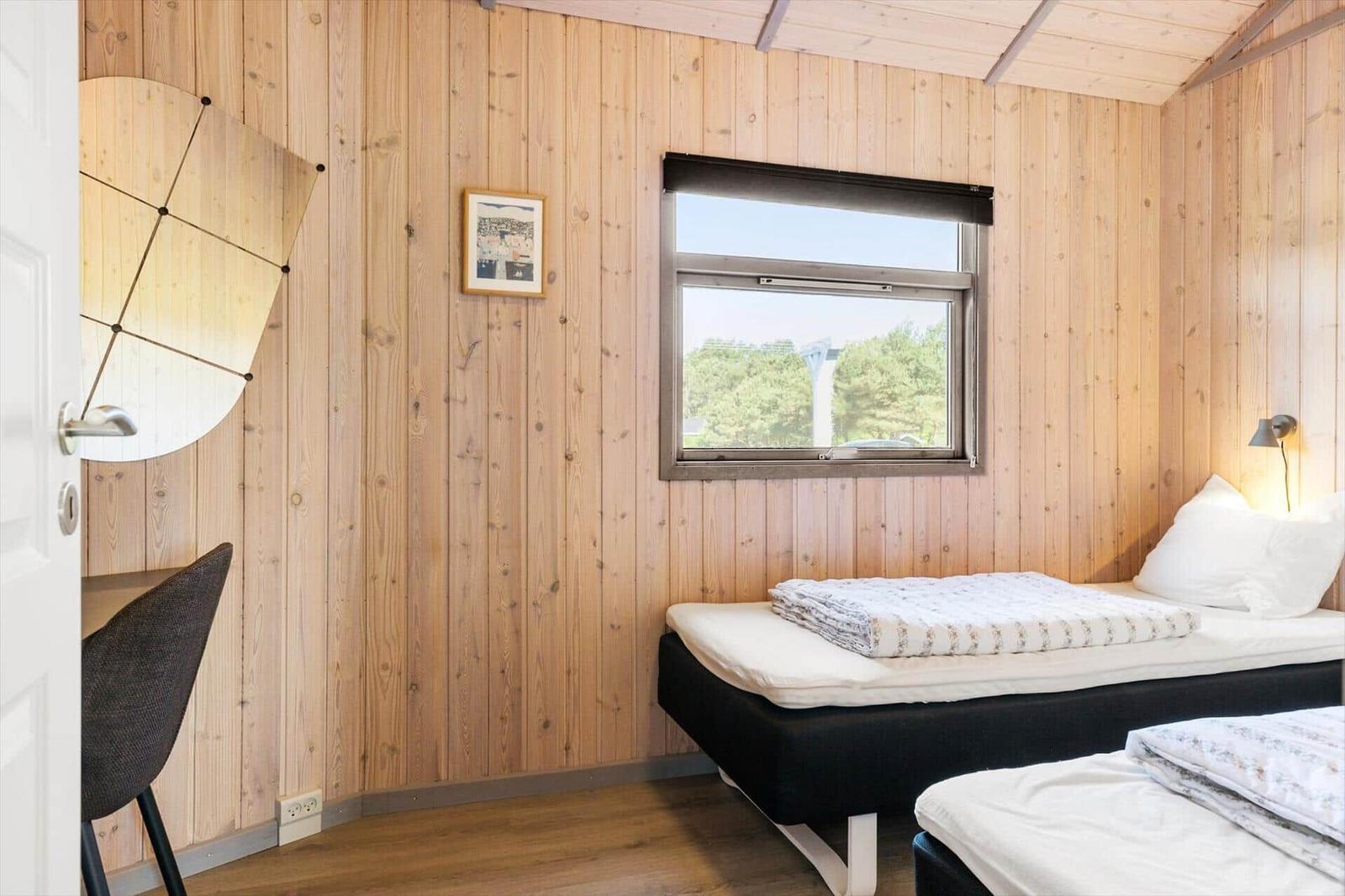 Zimmer mit Holzwand, Fenster, Bett und Schreibtisch