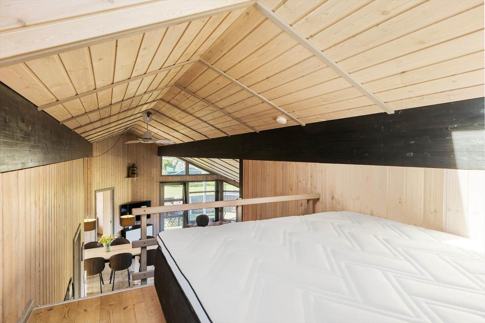 Schlafzimmer mit Bett und Blick in Wohnbereich mit Holzwand und Dach