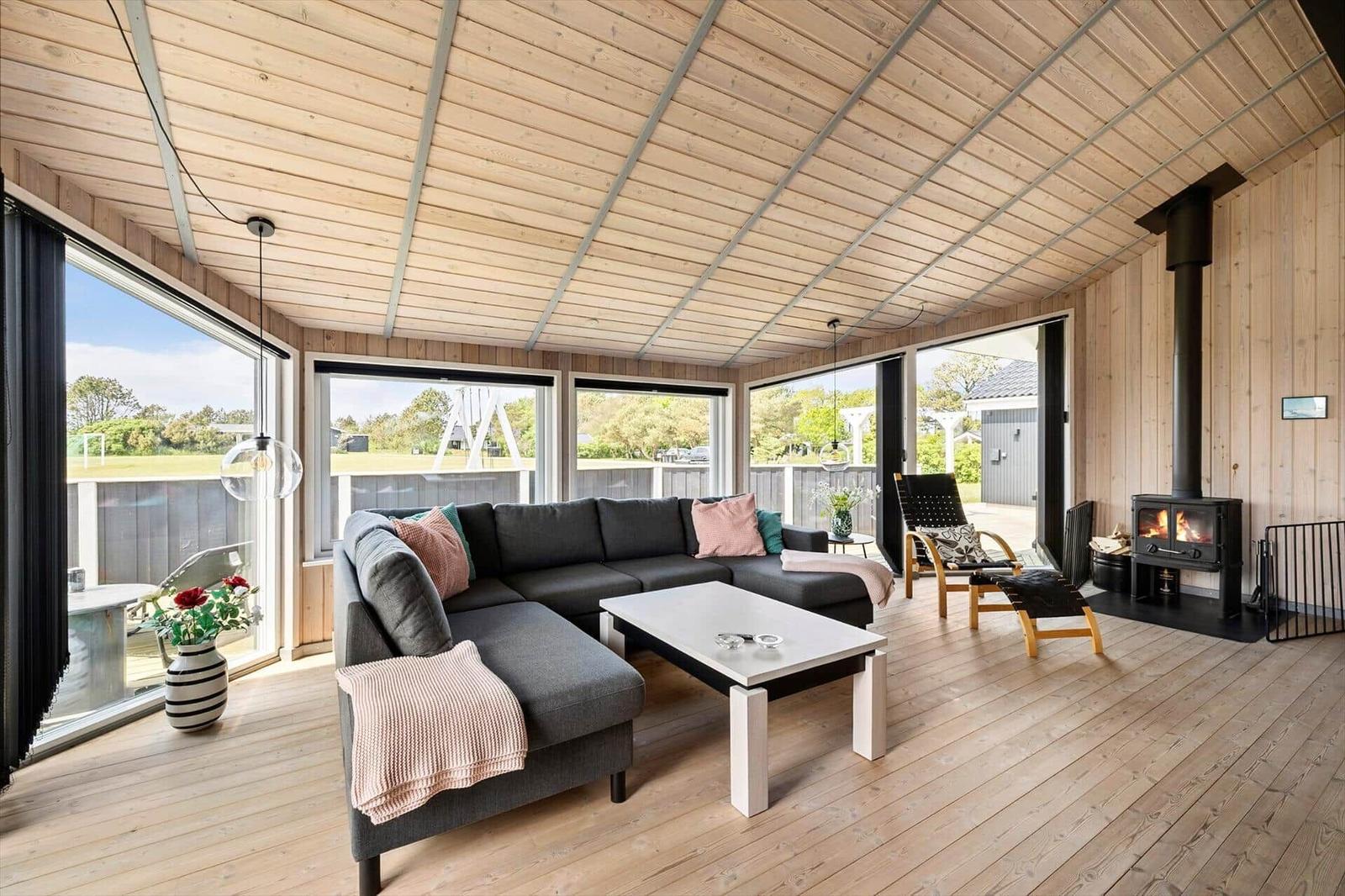 Wohnzimmer mit Sofa, Kamin und großen Fenstern. Holzboden und Holzwände.