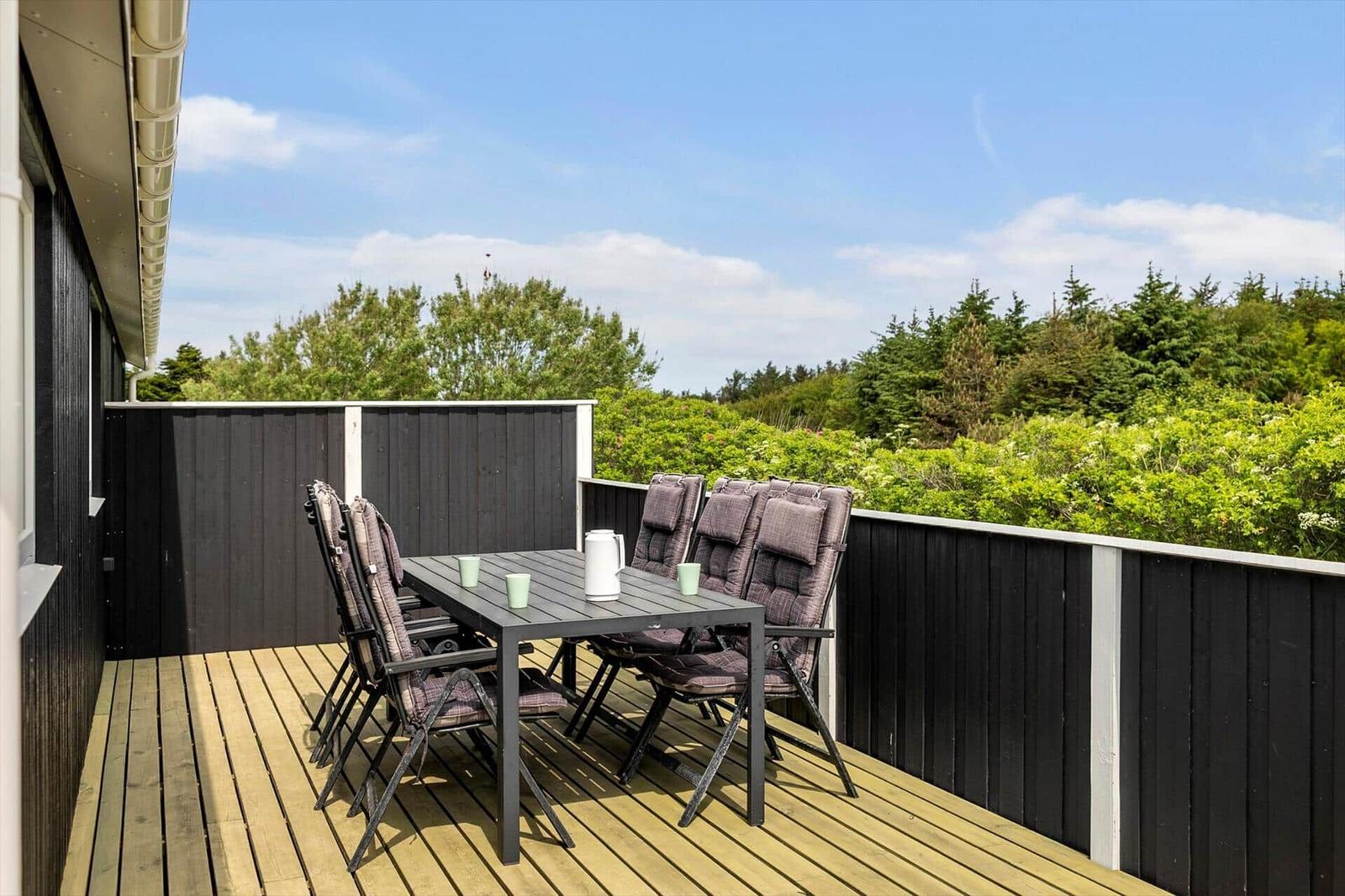 Terrasse mit Tisch und Stühlen, Blick auf grüne Bäume und Himmel.