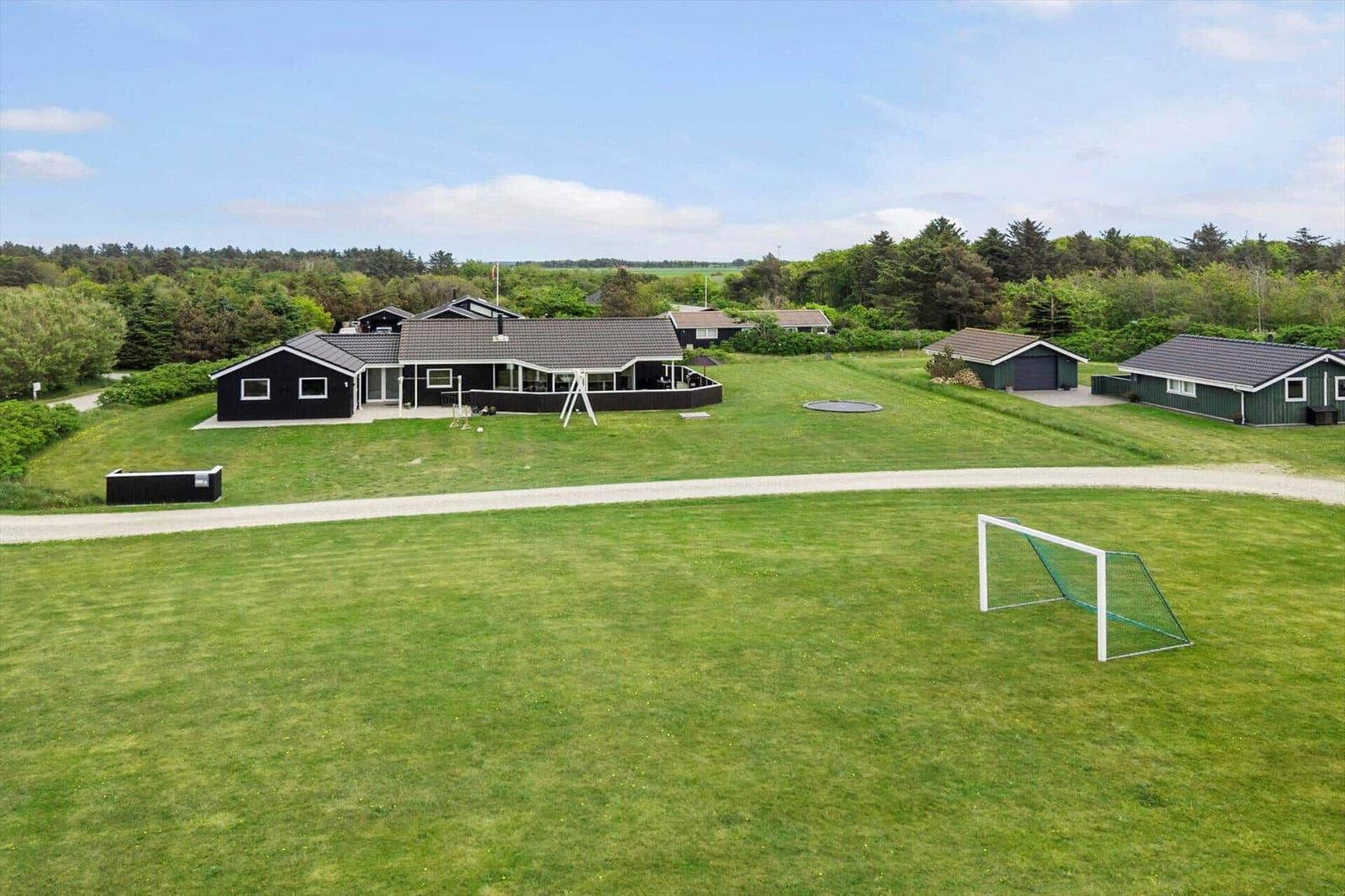 Grüner Rasen mit Fußballtor, mehrere Häuser und Bäume im Hintergrund.