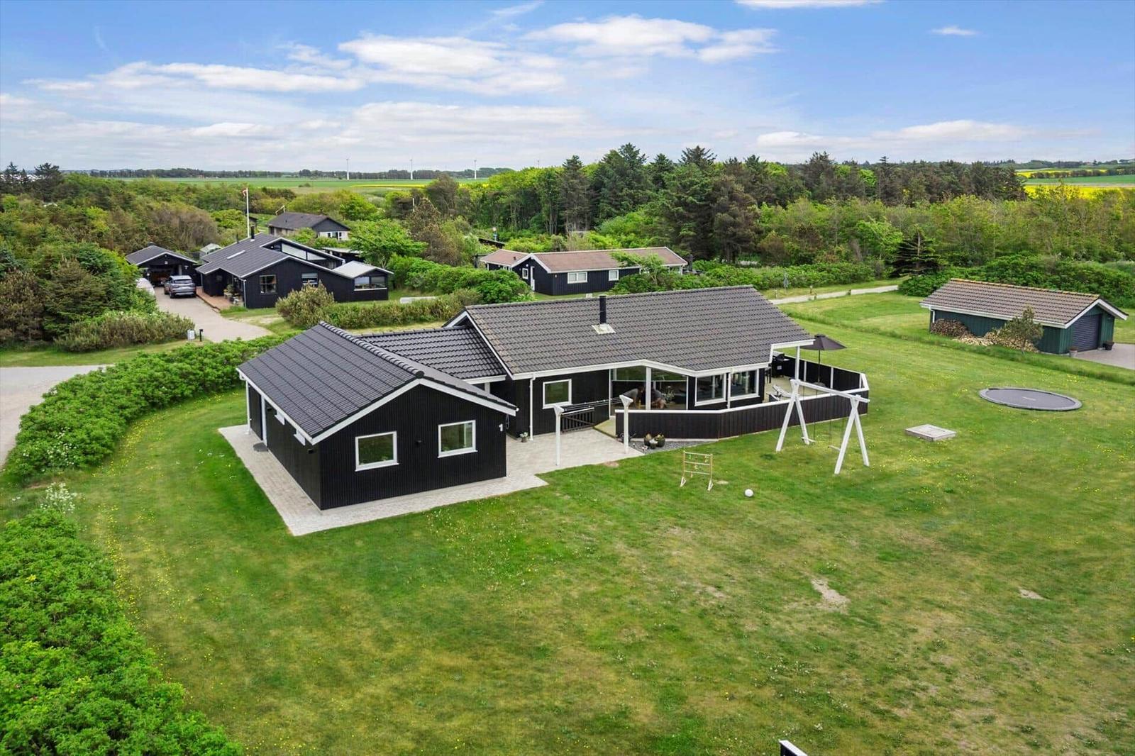 Schwarzes Holzhaus mit großem Garten und Terrasse. Trampolin und Schaukel im Freien.