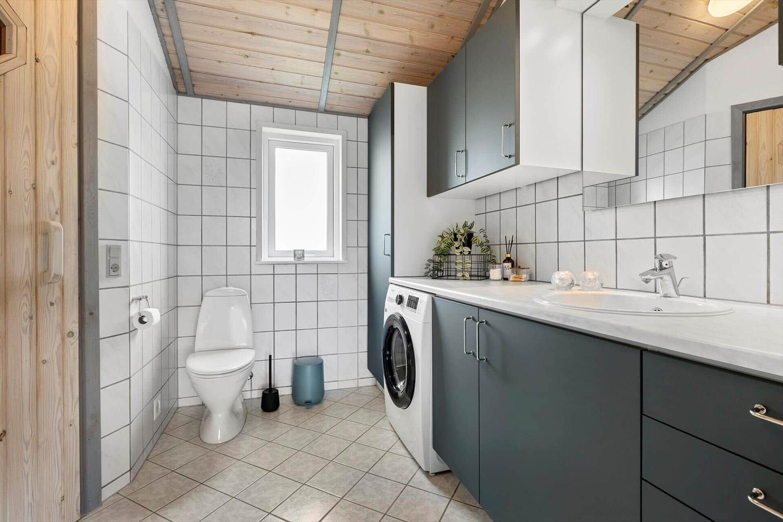 Badezimmer mit Toilette, Waschmaschine und Waschbecken unter grauen Schränken.