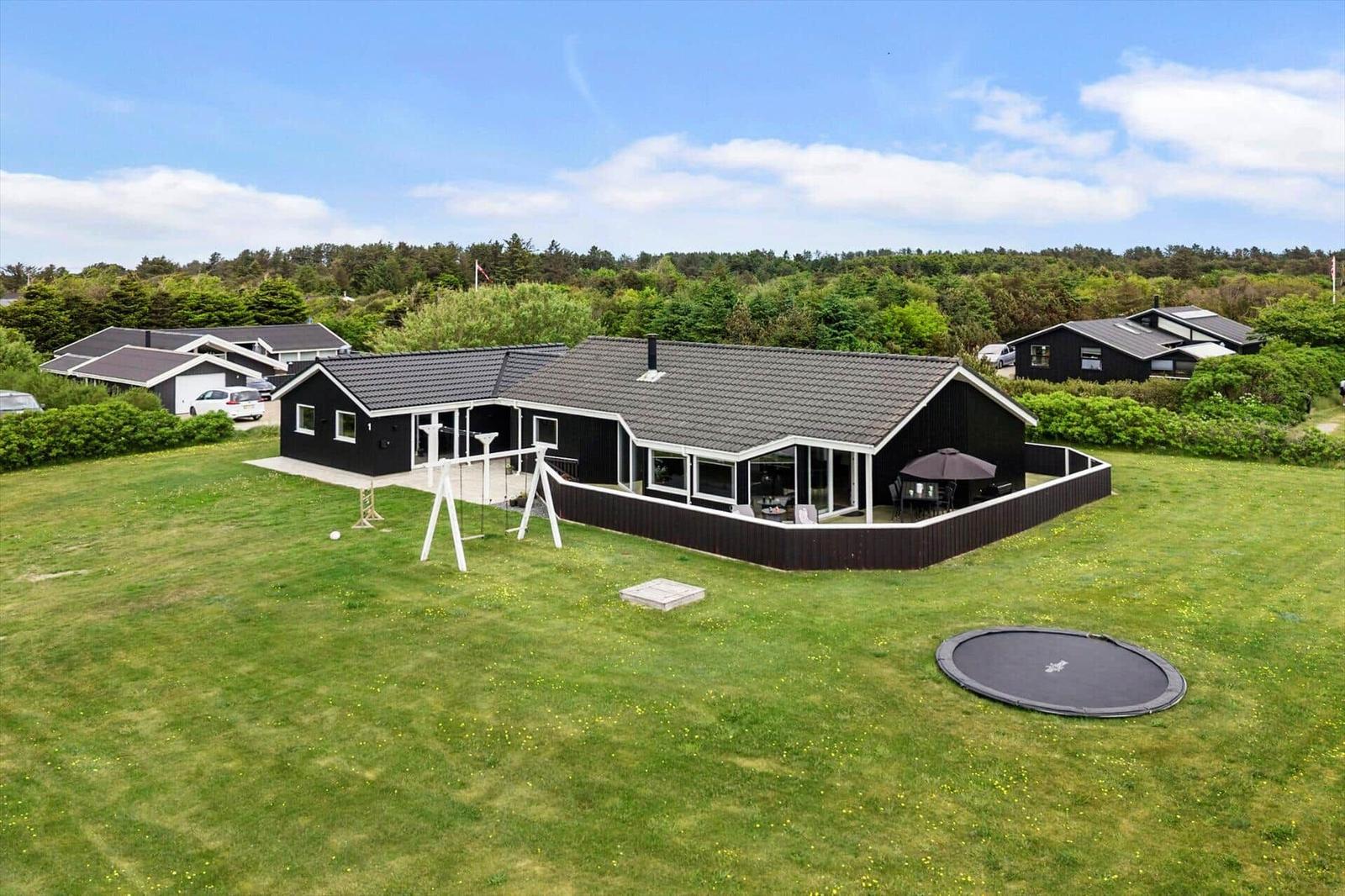 Schwarzes Haus mit großem Garten, Trampolin und Spielgeräten. Terrasse mit Sitzgelegenheiten.
