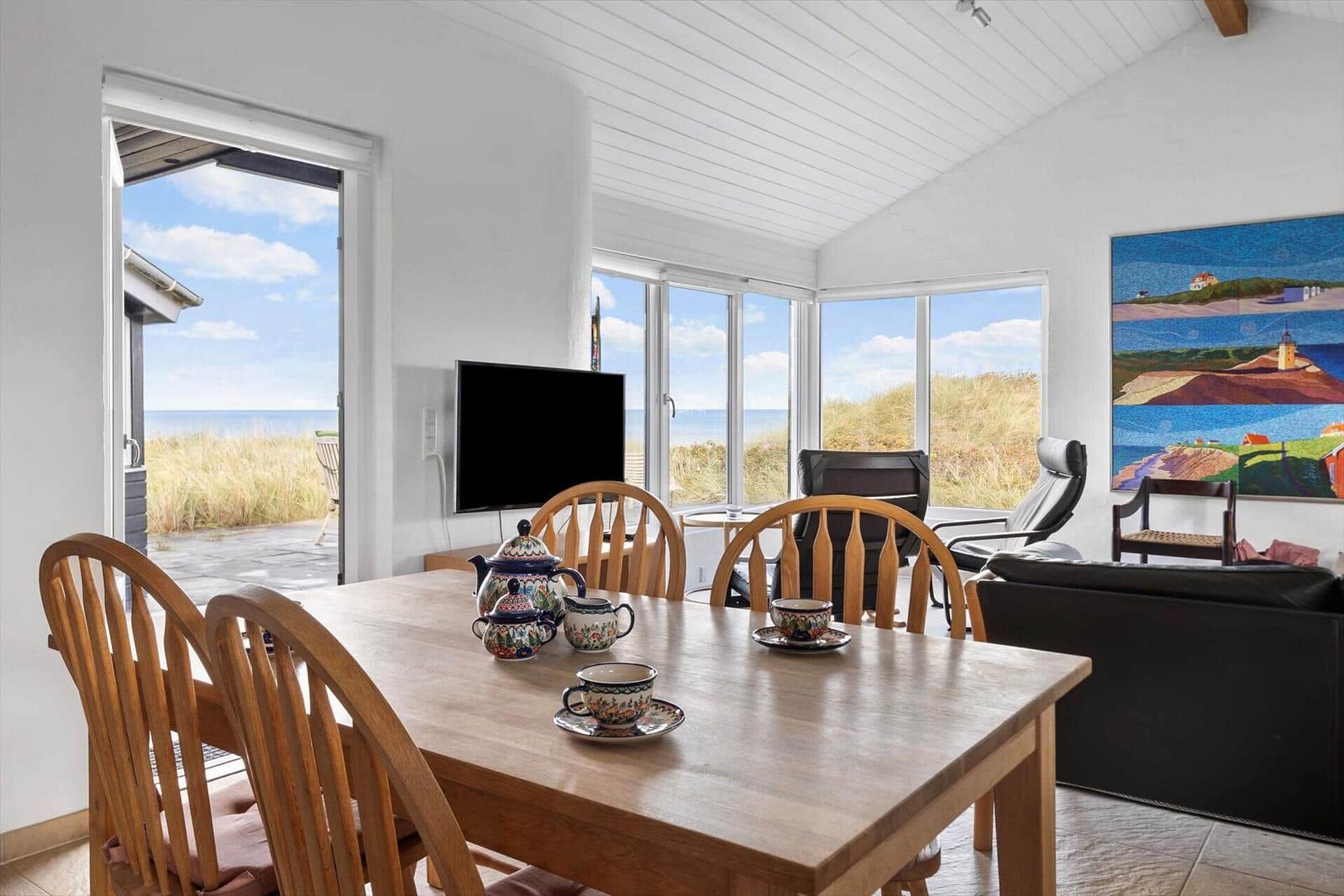 Esszimmer mit Holztisch, Stühlen und Meerblick durch große Fenster.