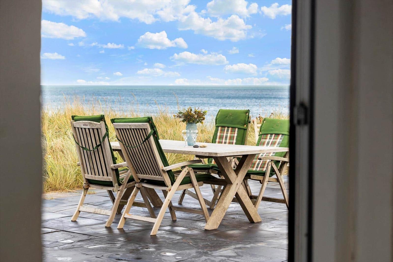 Terrasse mit Holztisch und Stühlen, Blick auf das Meer und Himmel.