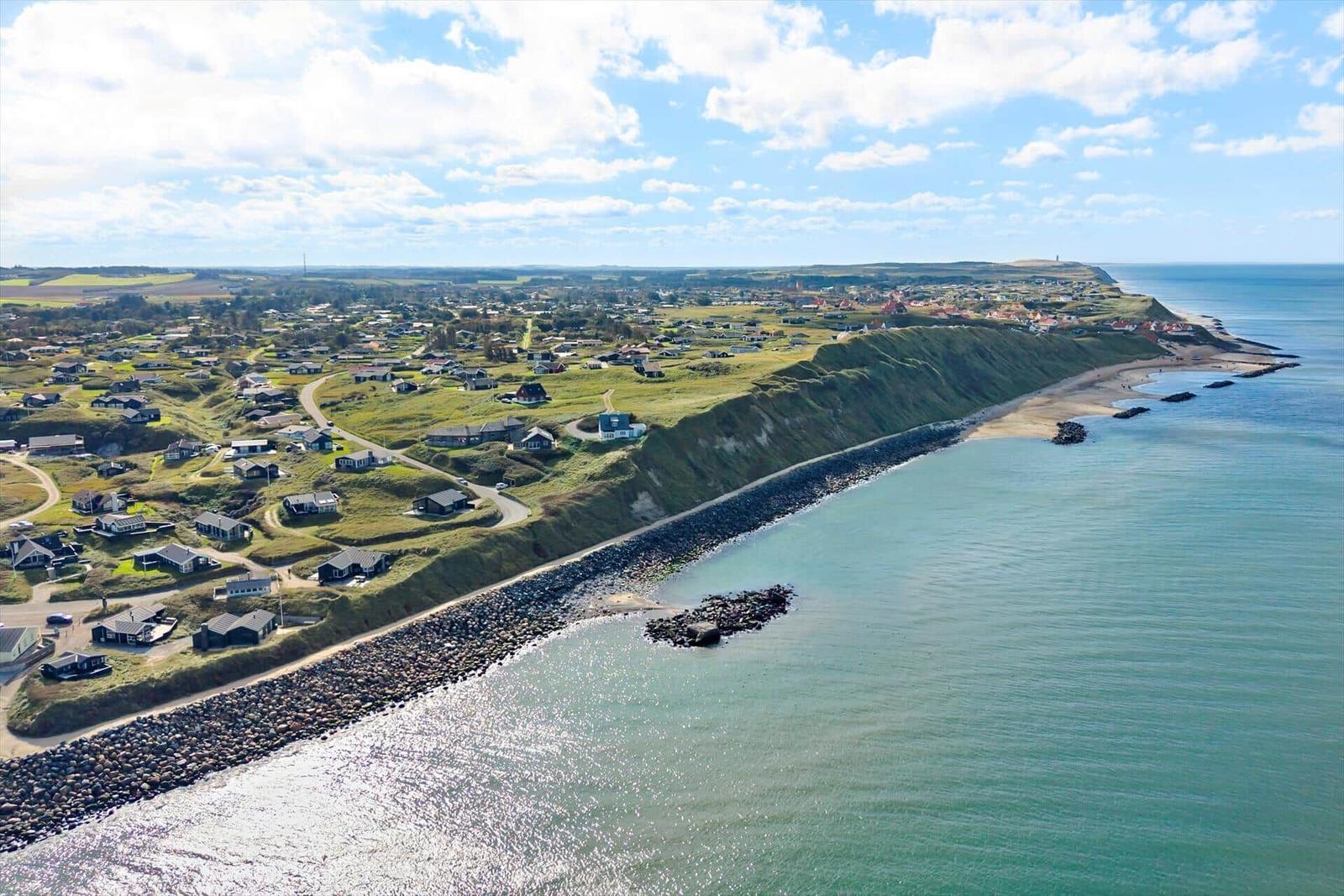 Aussicht auf Küstenort mit Grashügeln, Häusern und Steilküste am Meer.
