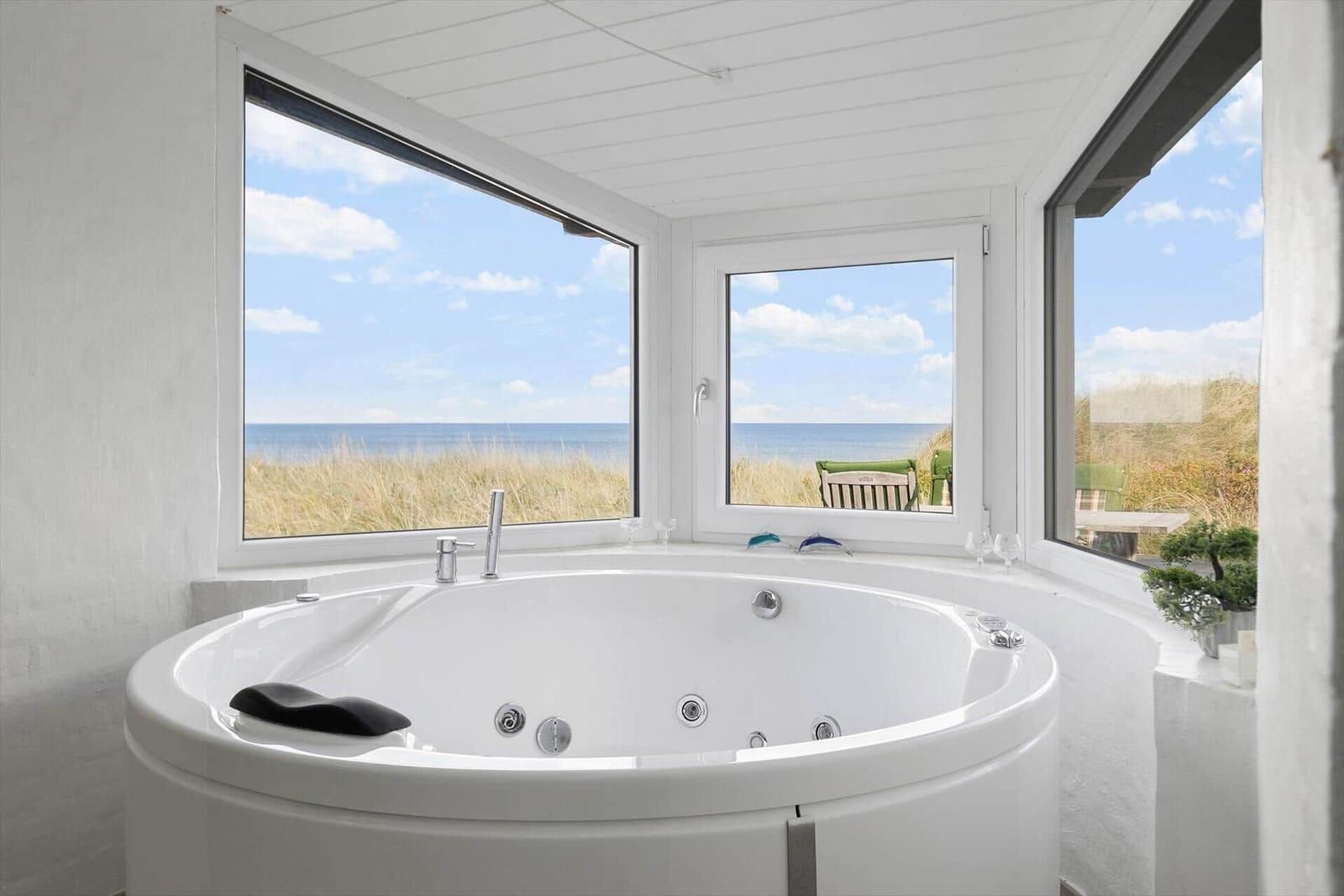Whirlpool mit Meerblick durch große Fenster im Badezimmer