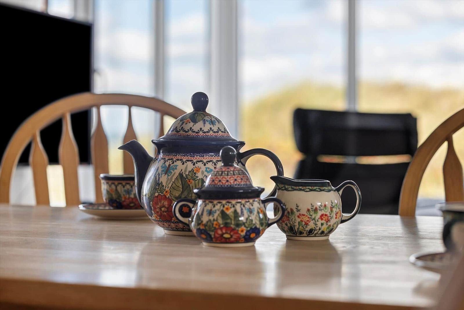 Teekanne, Tassen und Milchkanne mit floraler Keramik auf Holztisch.