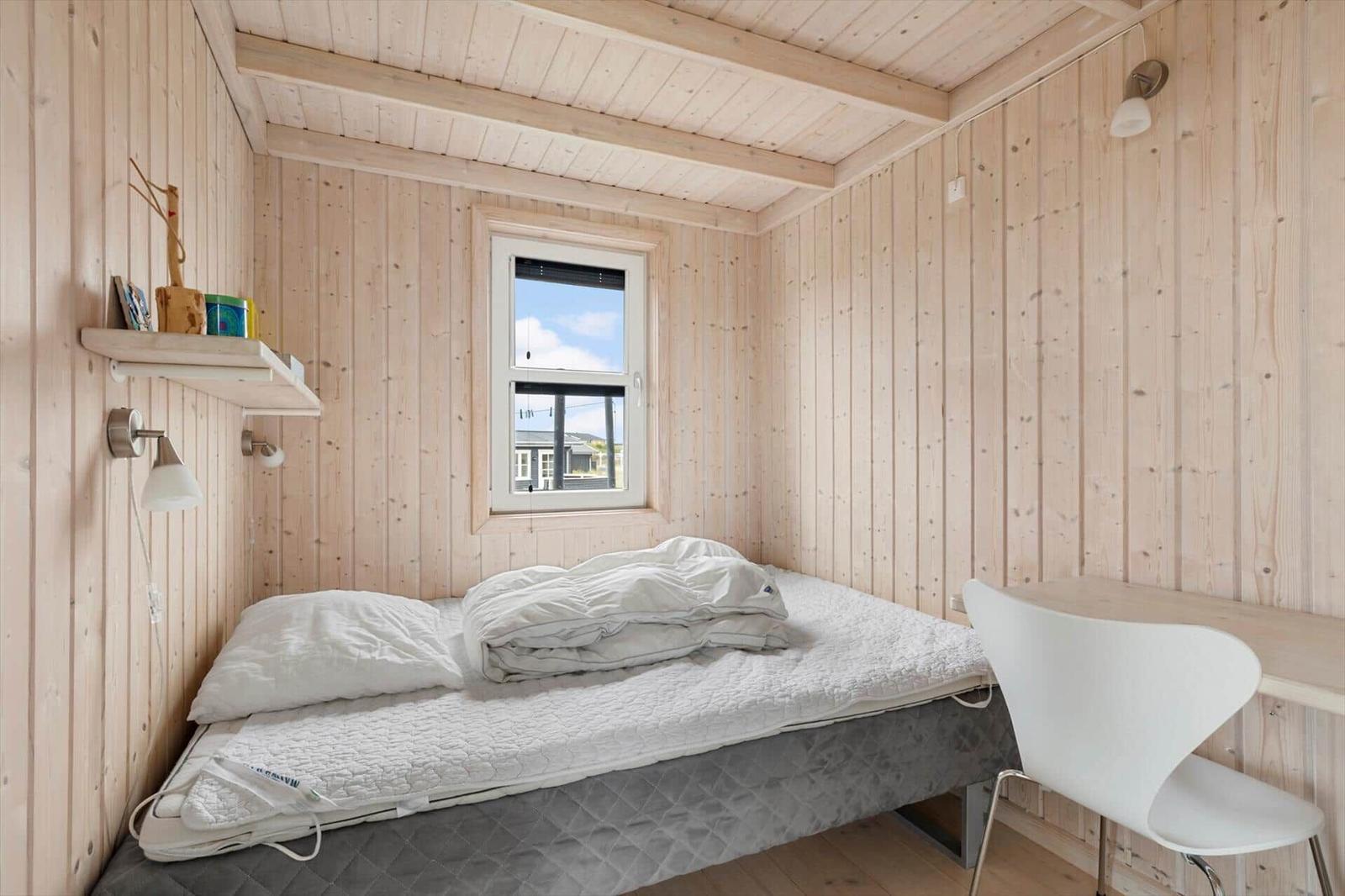 Ein Schlafzimmer mit Holzwand, Bett, Schreibtisch und Fenster.