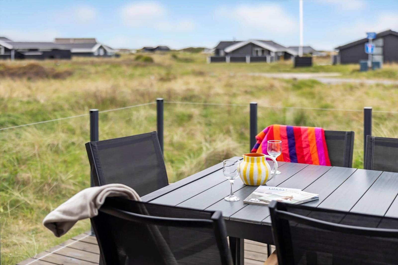 Terrasse mit Tisch und Stühlen, Blick auf Grasland und Häuser im Hintergrund.