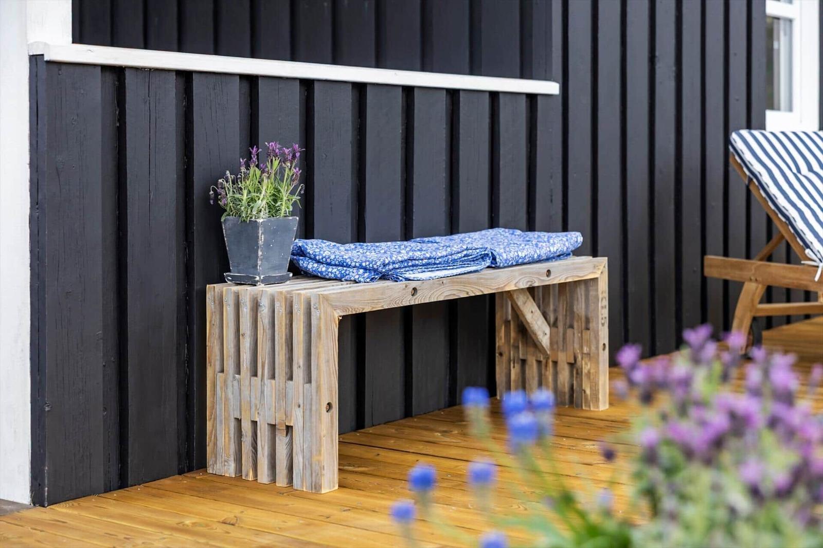 Holzbank mit blauer Decke und Lavendel vor schwarzem Hauswand