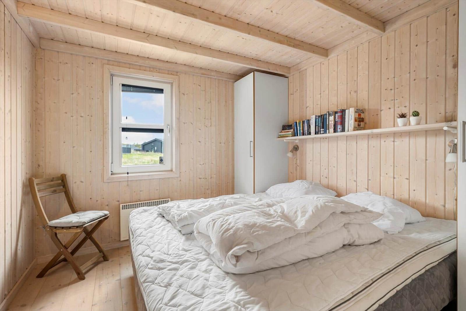 Schlafzimmer mit Holzwand, Bett, Stuhl und Bücherregal.