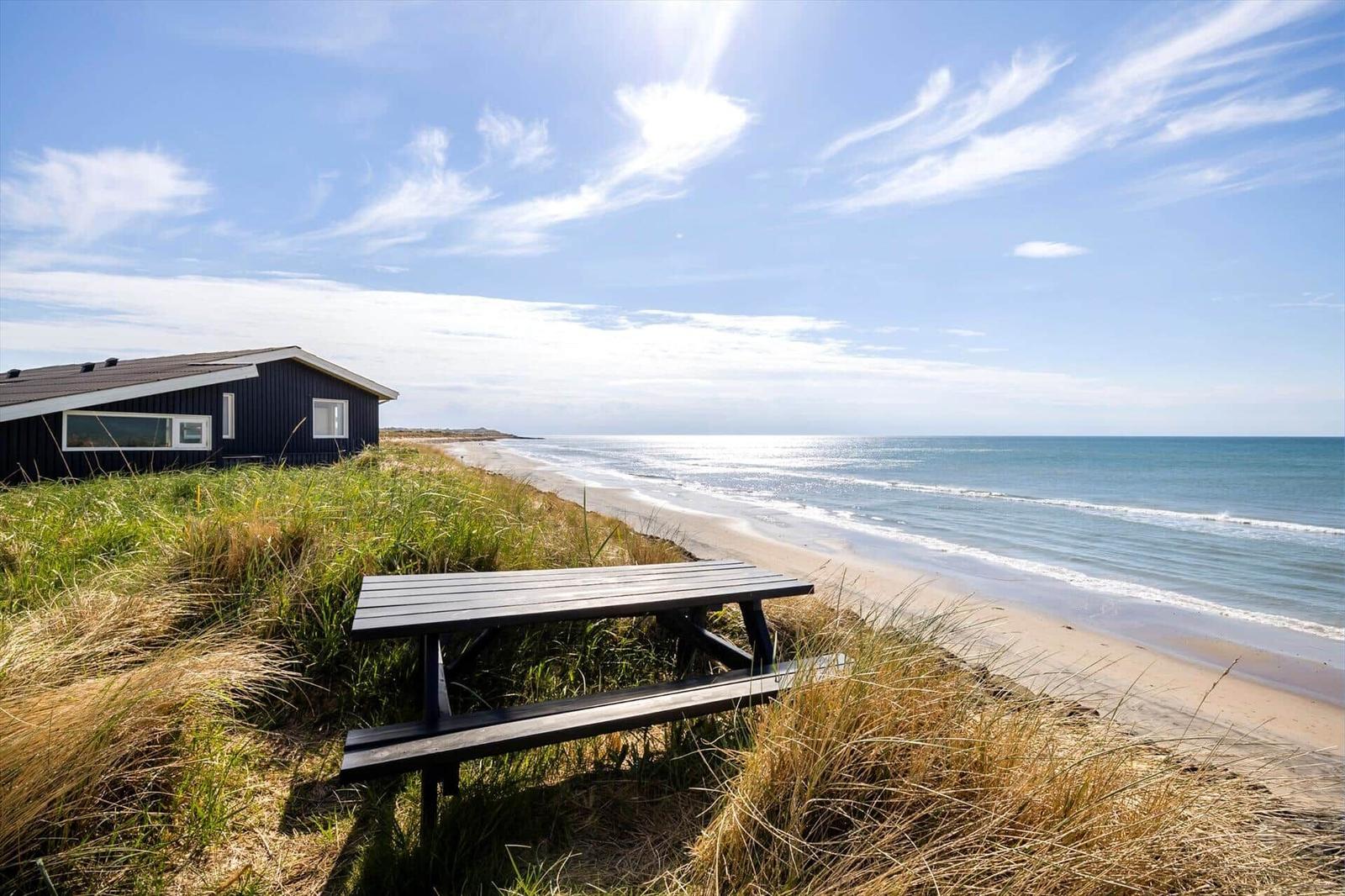 Schwarzes Strandhaus mit Picknicktisch zwischen Dünen und Meer.