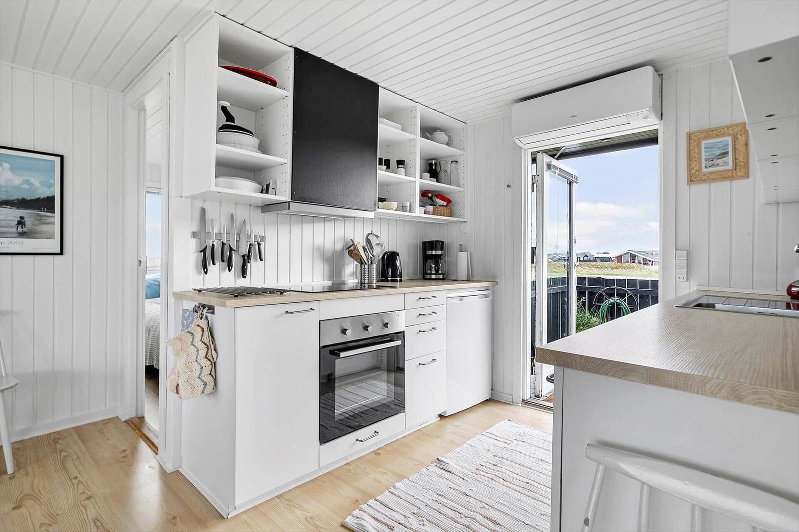 Küche mit weißen Schränken, Holzoberflächen und Blick auf Balkon.