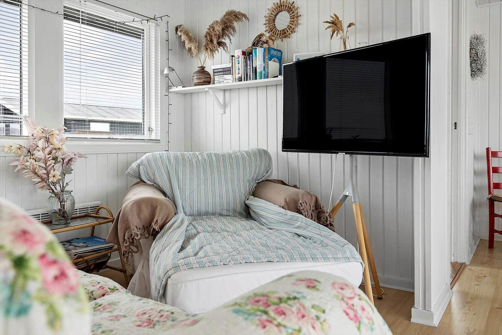 Ein Wohnzimmer mit Sessel, Fernseher und Fenster mit Jalousien.