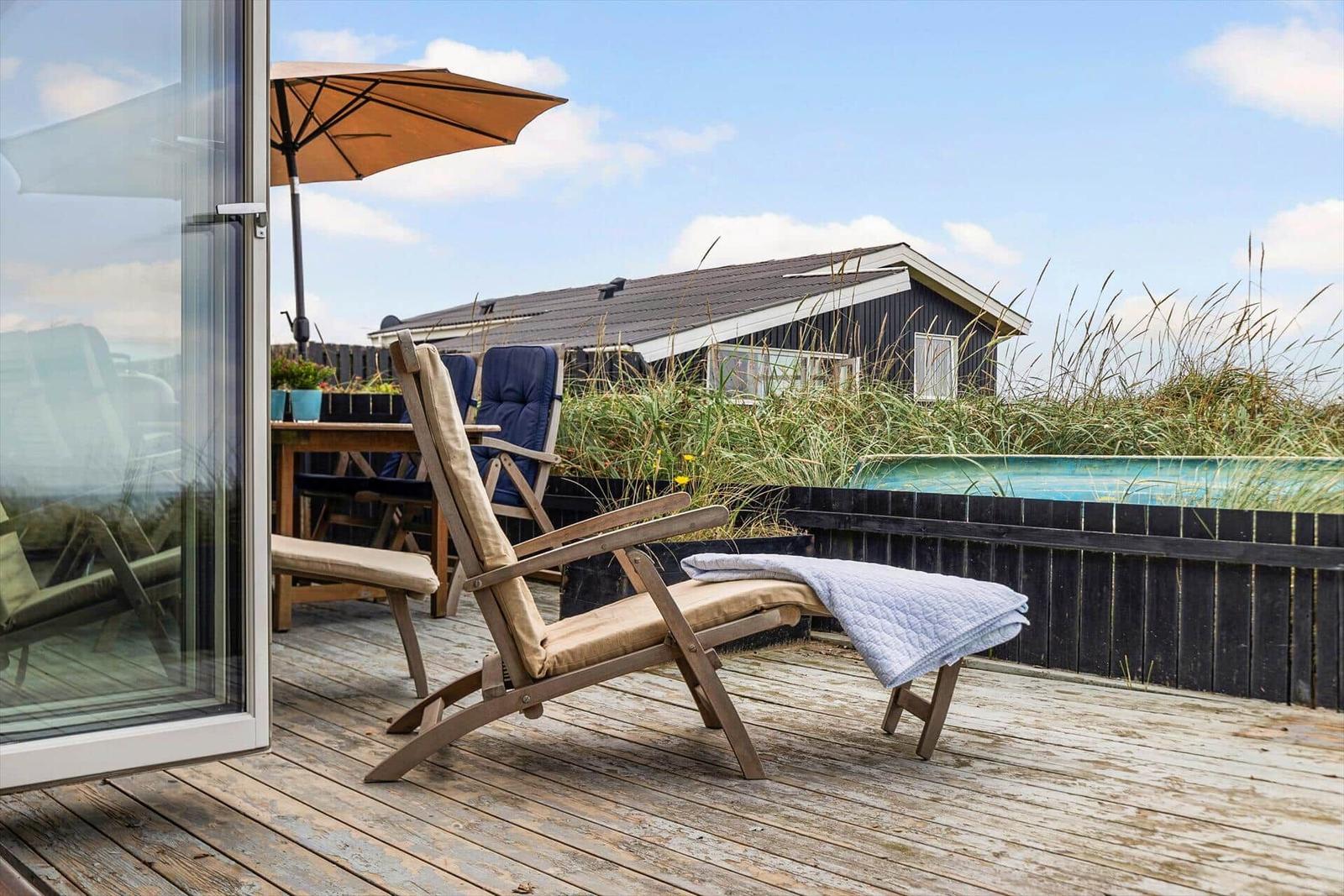 Terrasse mit Liegestuhl, Sonnenschirm und Blick auf Strandhaus