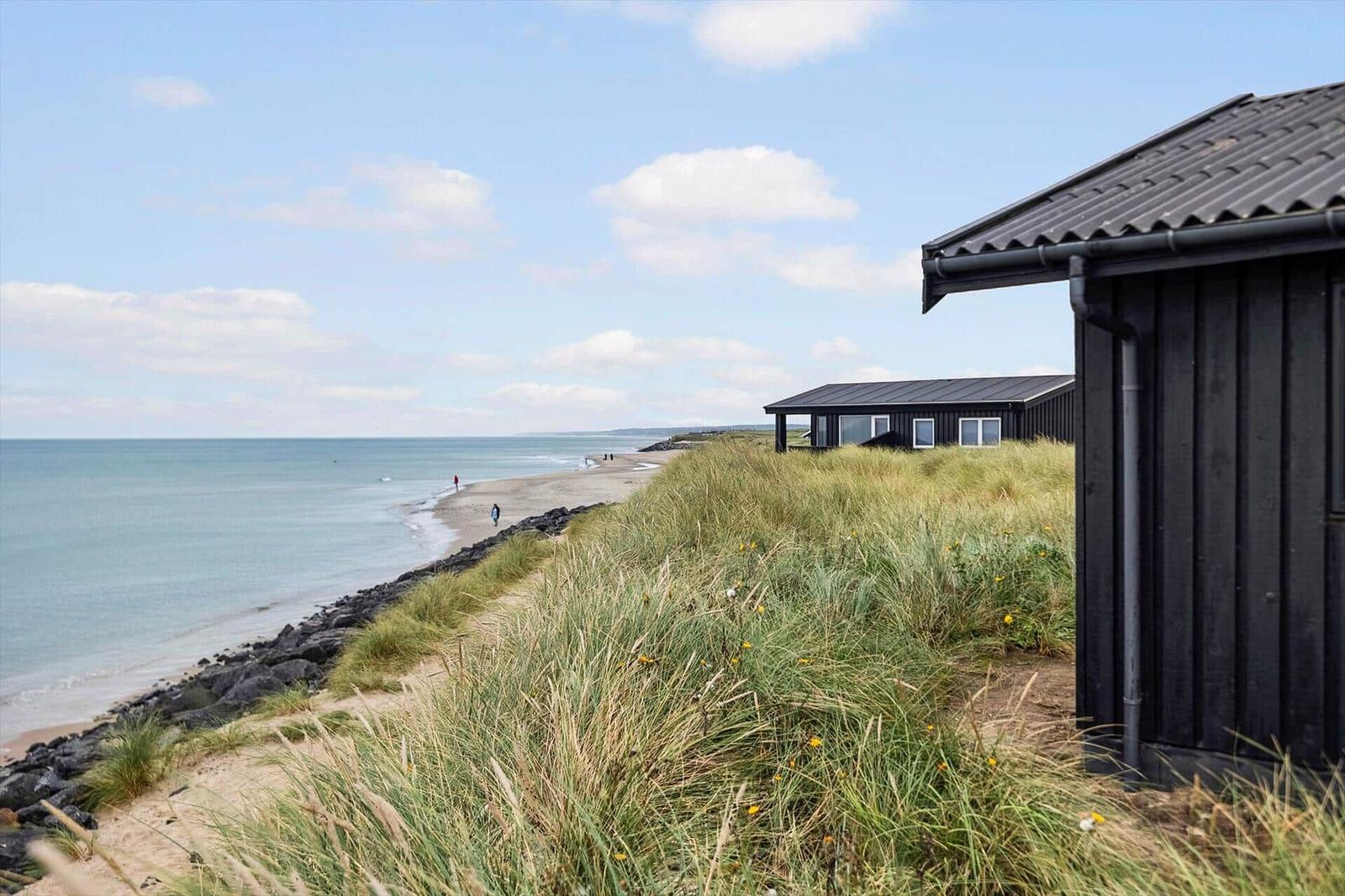 Schwarzes Strandhaus auf Dünen mit Blick auf das Meer und Strand.
