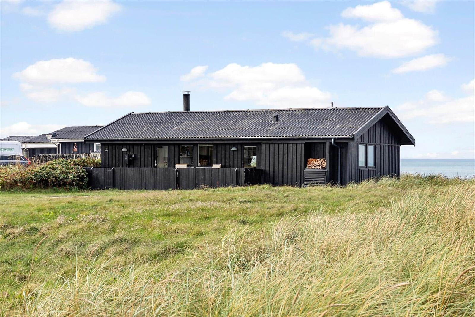 Schwarze Holzhütte am Strand mit Garten und Holzstapel. Blick auf das Meer.